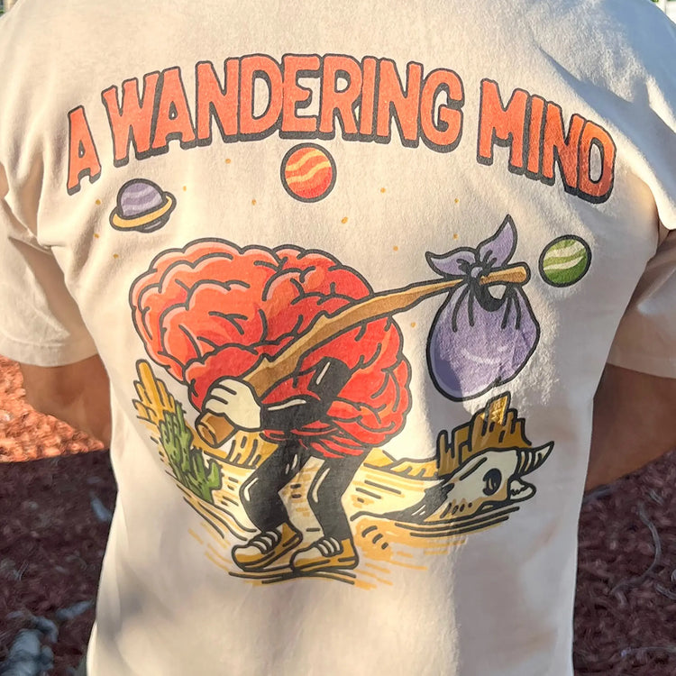 A Wandering Mind Arid Thoughts t-shirt in sand back graphic featuring wandering brain character, desert, skull