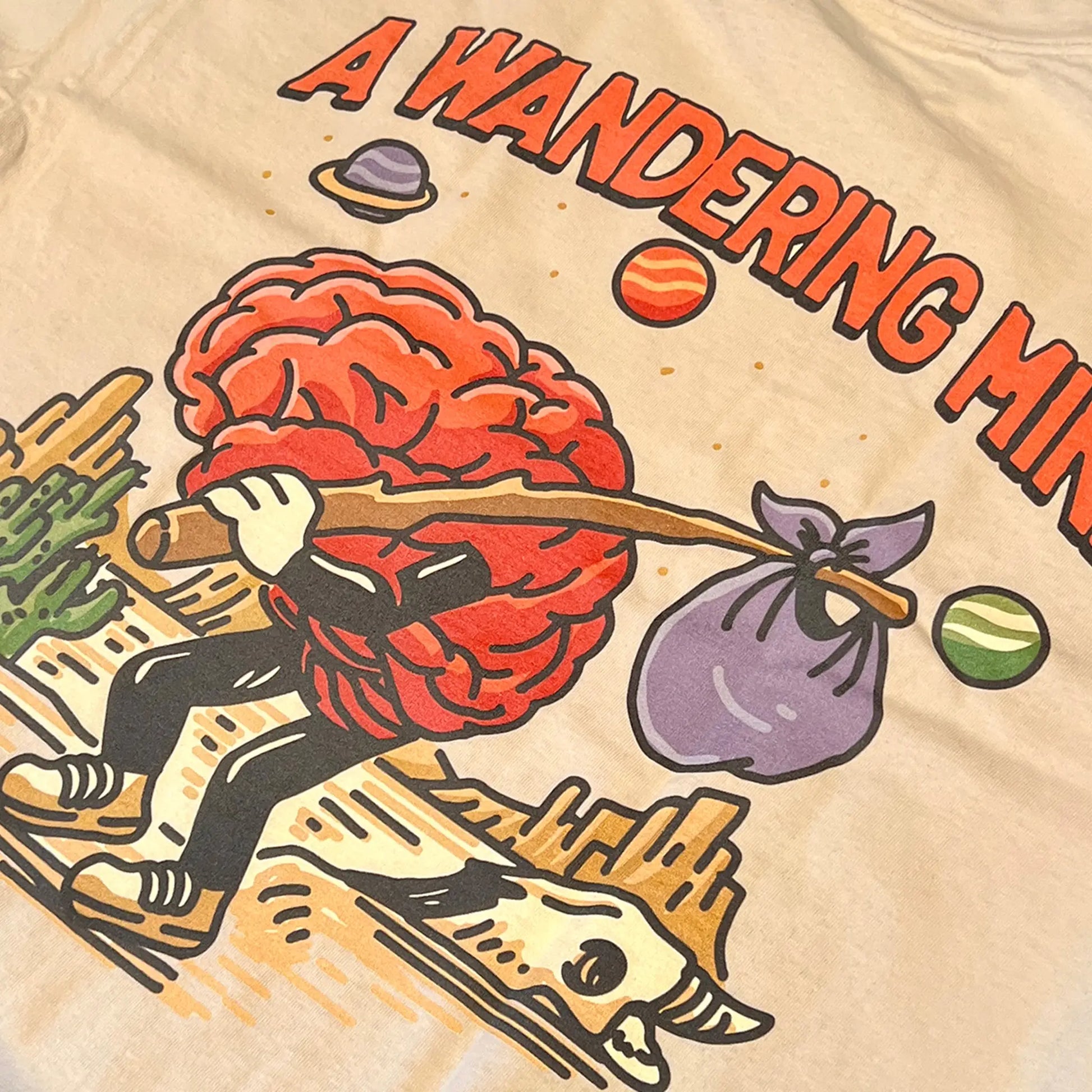 A Wandering Mind Arid Thoughts t-shirt in sand back graphic detail showing wandering brain character, desert, skull