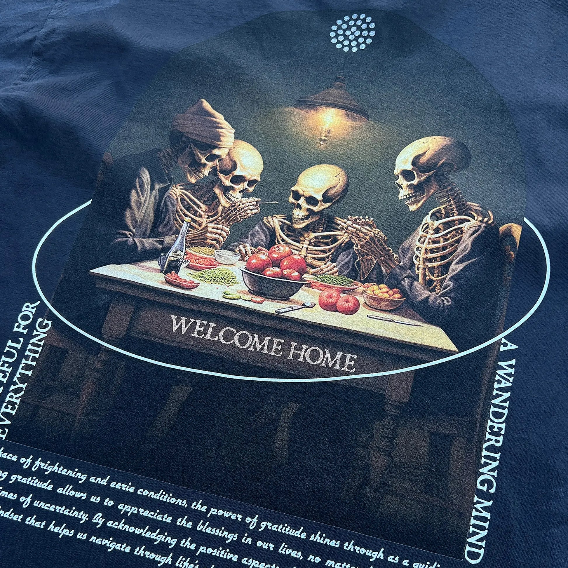 A Wandering Mind Grateful for Everything t-shirt in slate back graphic detail showing skeletons at table, food, interior scene