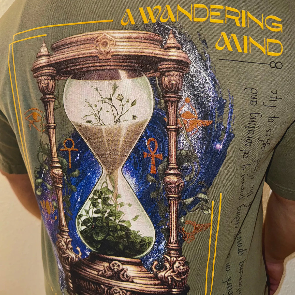 A Wandering Mind Growth & Renewal t-shirt in olive back graphic featuring hourglass, foliage, symbolic elements