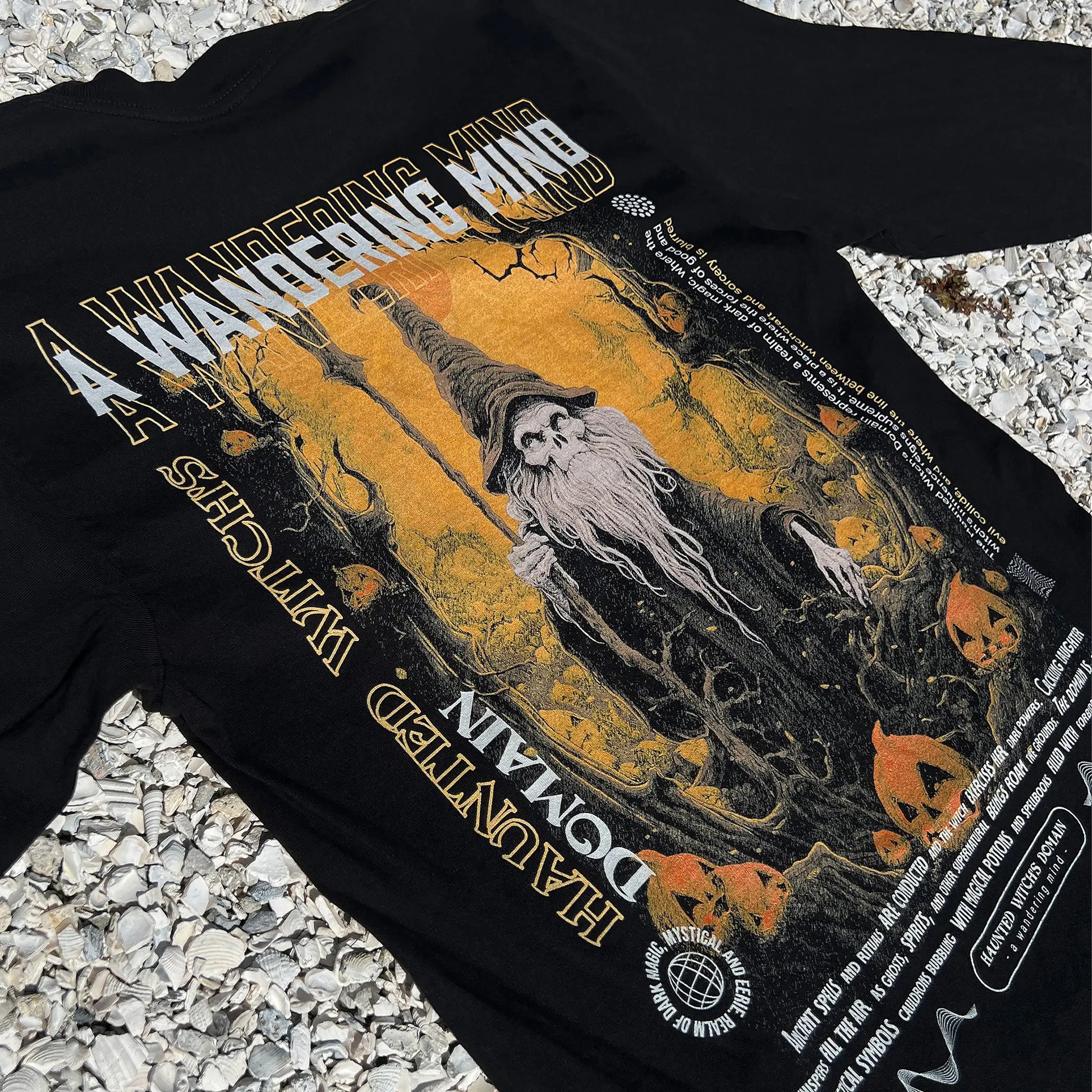 A Wandering Mind Haunted Witch's Domain long sleeve t-shirt in black back graphic angled view of skeletal wizard, jack-o’-lanterns, forest