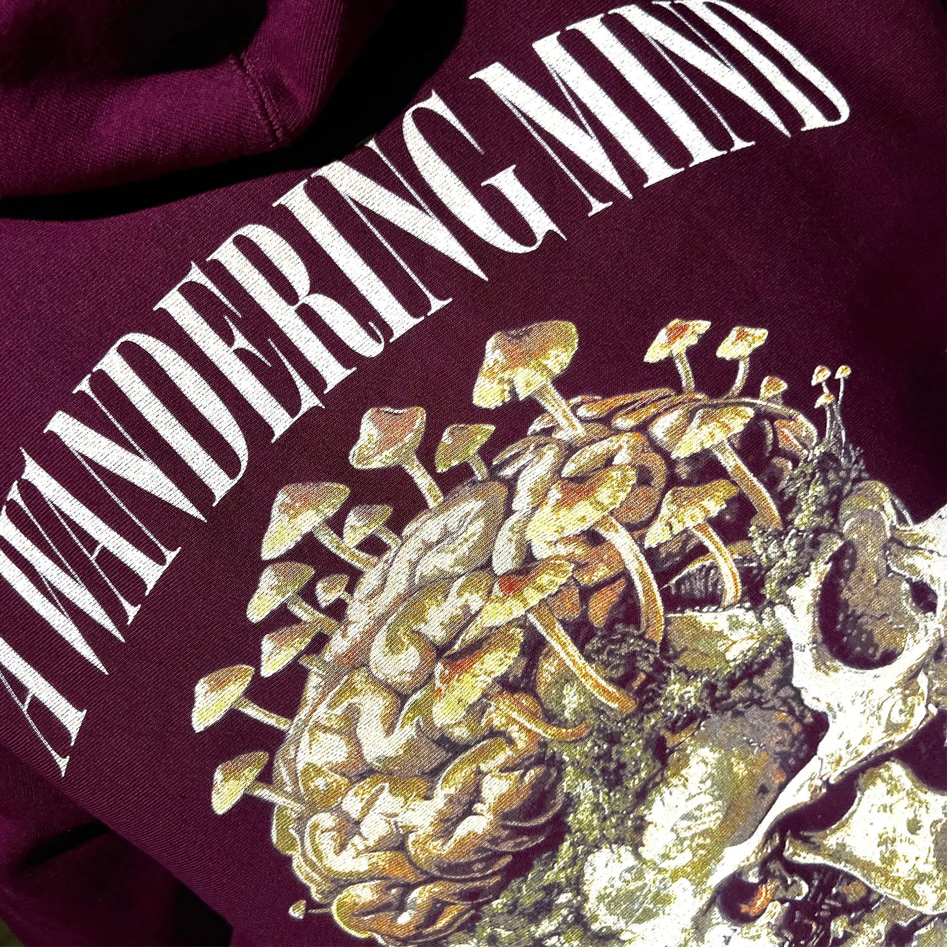 A Wandering Mind Rebirth hoodie in maroon back graphic angled view of skull, mushrooms, moss